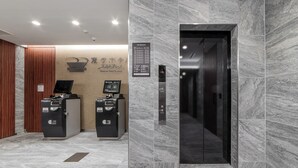 Un área de ascensores moderna con paredes de mármol y un panel informativo digital.