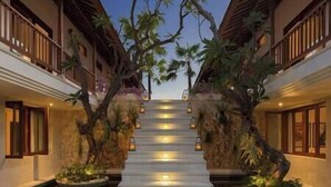 Ein Hotelkorridor mit einer zentralen Treppe, die von Bäumen und Laternen gesäumt wird und zu einem Balkon im zweiten Stock führt.