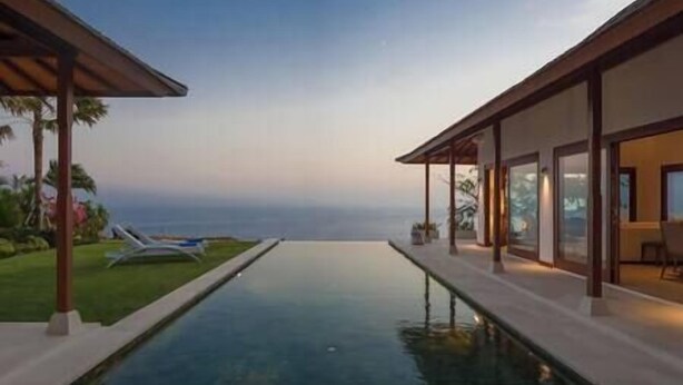 Ein moderner Poolbereich mit freiem Blick auf den Ozean, umgeben von einer gepflegten Rasenfläche und Liegestühlen.