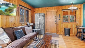 A cozy cabin interior with a wooden interior, a sofa, a table, and a refrigerator. - Timber Lodge Cabins 29 (Colorado Springs)