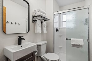 A bathroom with a white sink, toilet, and glass shower door. There are towels on a rack and a mirror above the sink. - Timber Lodge Cabins 29 (Colorado Springs)