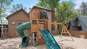 A playground with a slide and a swing set, surrounded by wooden cabins. - Timber Lodge Cabins 29 (Colorado Springs)