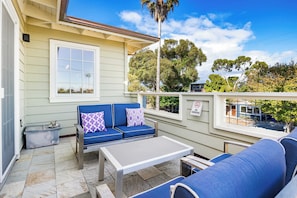 A covered outdoor seating area with a blue sofa, a small table, and a view of trees and a building in the background.