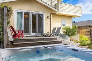 A backyard with a hot tub, a covered patio with chairs, and a sliding glass door.