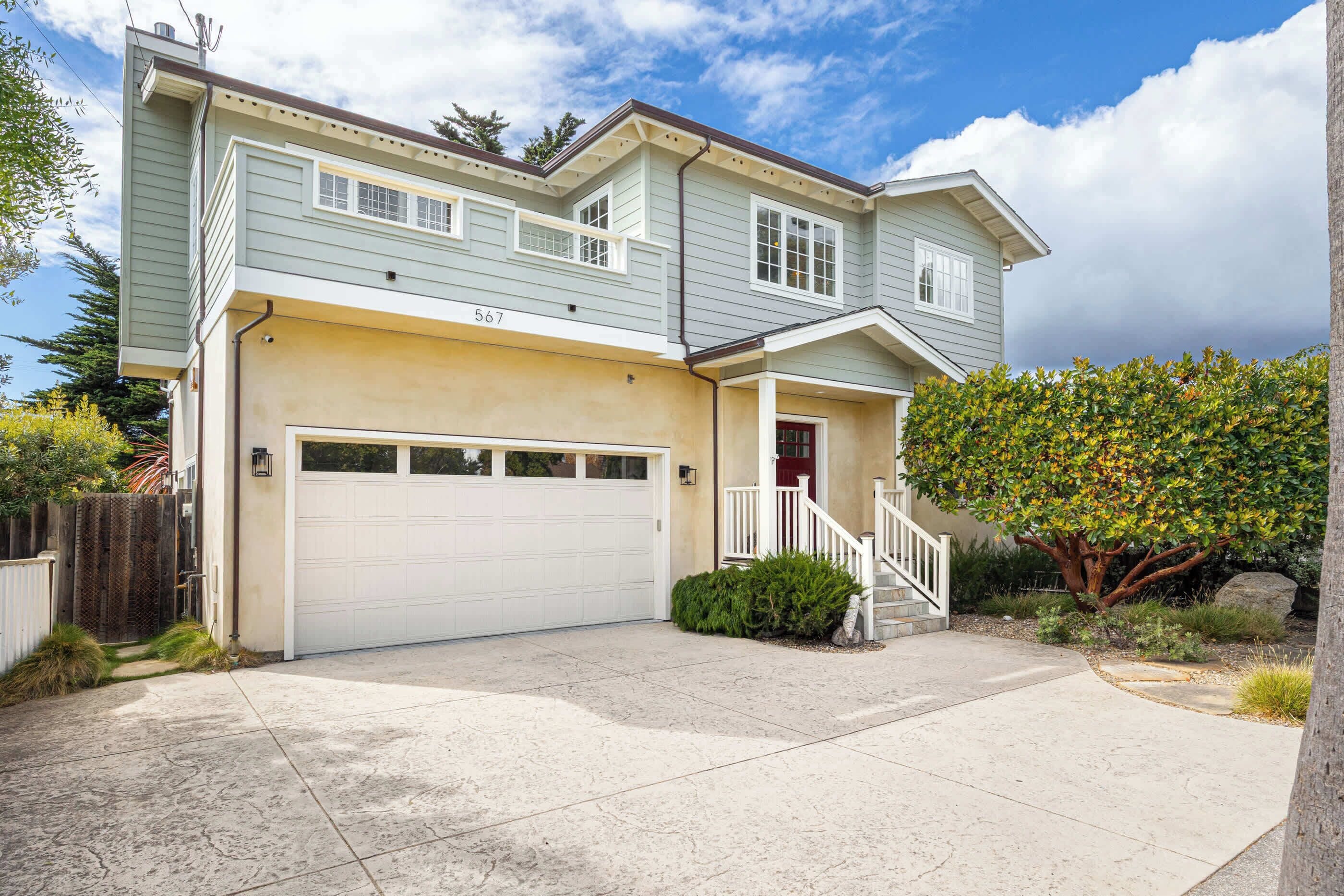 A two-story house with a garage, a red door, and a staircase leading to the front porch.