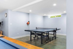 A ping pong table in a room with light blue walls, a clock on the wall, and a small window with greenery visible. - Gorgeous Pleasure Point Home - Sleeps 10! (Santa Cruz)