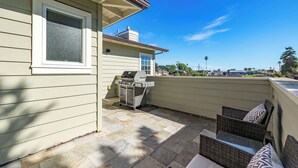 A patio with a grill, wicker furniture, and a view of a city skyline.