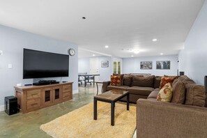 A living room with a flat-screen TV, wooden entertainment unit, brown sofa, and a coffee table. - Gorgeous Pleasure Point Home - Sleeps 10! (Santa Cruz)