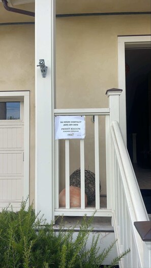 Una casa con porche blanco, un cartel que indica contacto las 24 horas y un número de permiso.