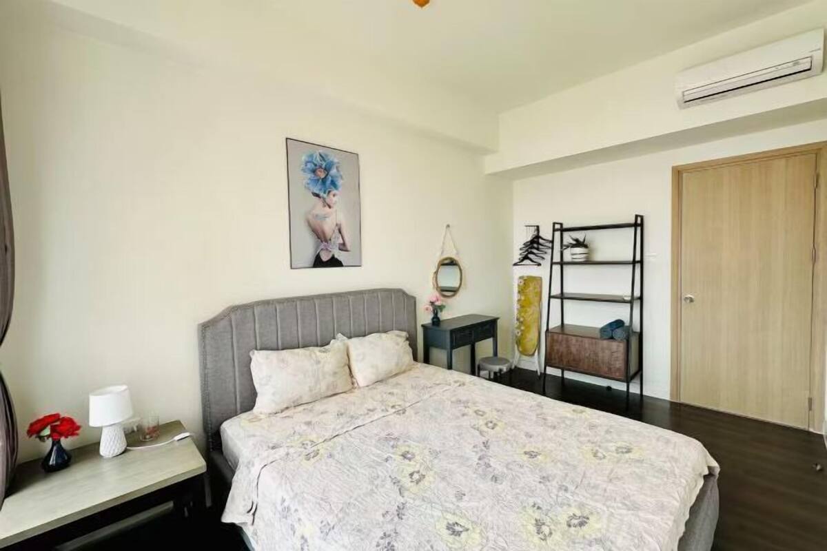 A bedroom with a bed, bedside table, lamp, and a wall-mounted shelf with a mirror and decorative items.