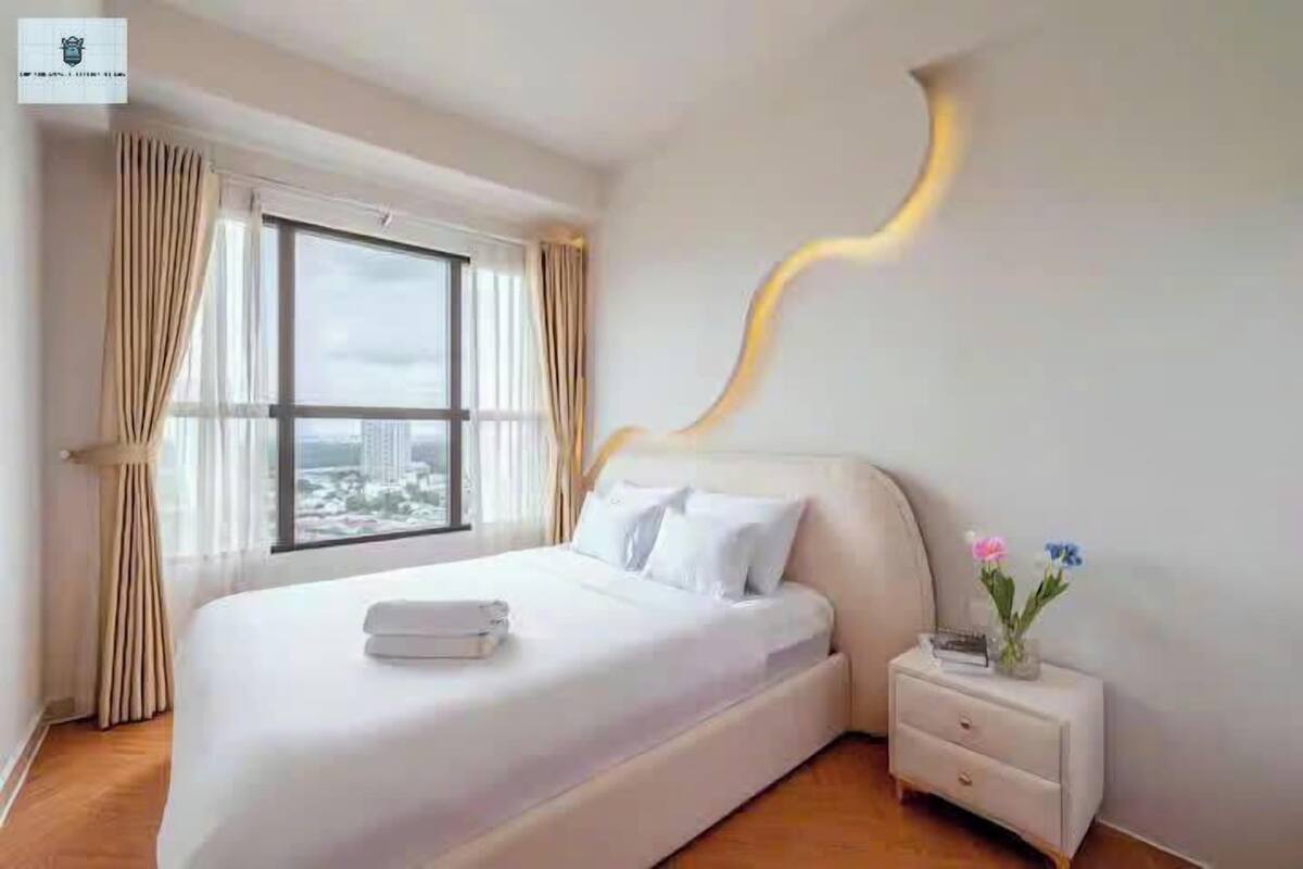A modern hotel room with a large bed, a nightstand, and a view of the city through the window.