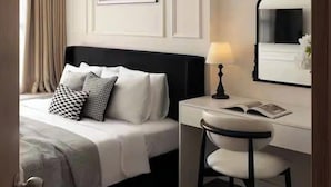 Habitación de hotel con una cama bien hecha, un escritorio con silla, una lámpara y un cuadro en la pared.