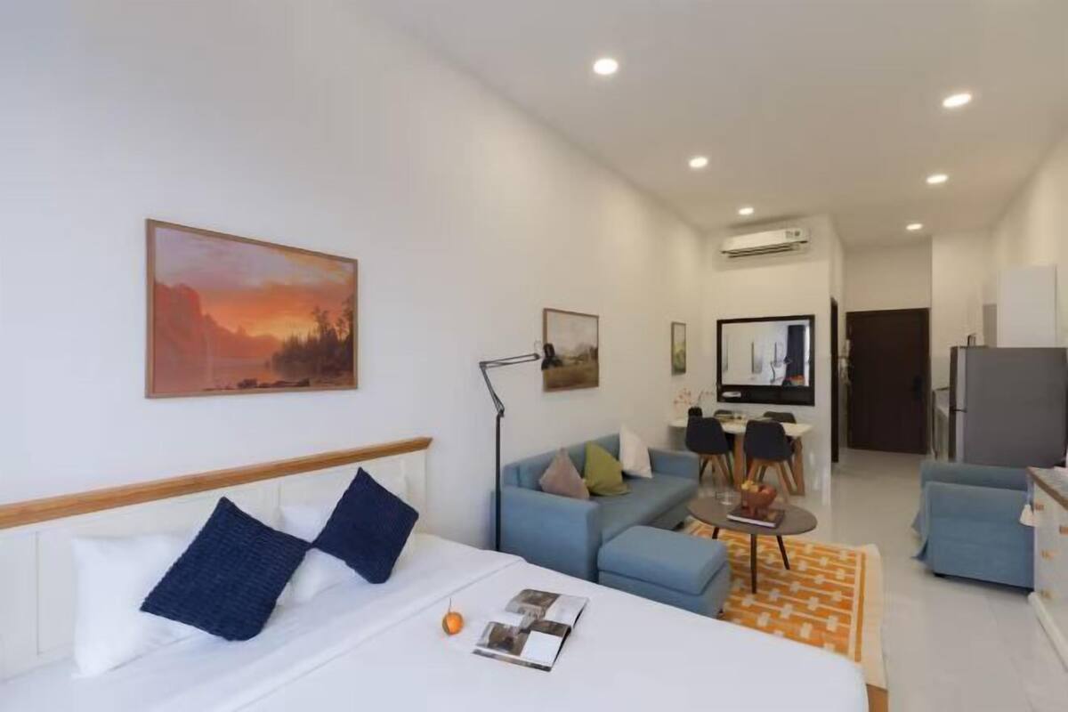 A modern hotel room with a bed, a sofa, a dining table, and a TV.