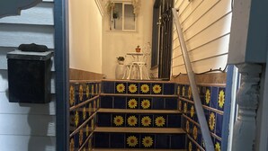 Un escalier dont les carreaux sont ornés d’un motif de tournesols bleus et jaunes, une chaise blanche et une petite table sur laquelle est posée une plante en pot.