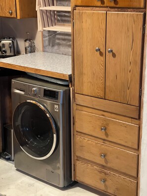 A compact laundry area with a front-loading washing machine, wooden cabinets, and a countertop.