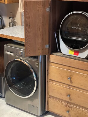A compact washer and dryer unit with a wooden cabinet above it.