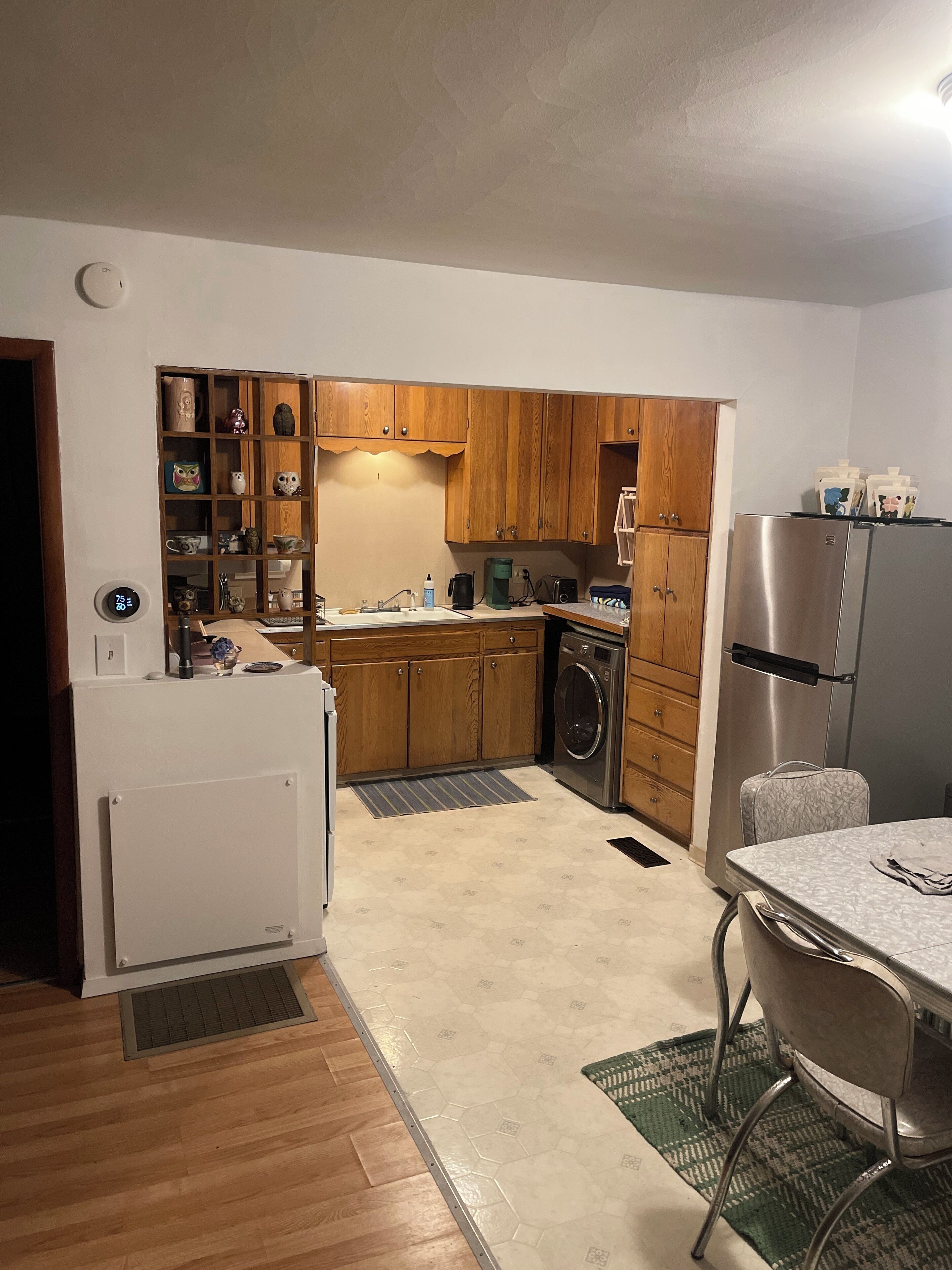 Una cucina compatta con mobili in legno, un frigorifero in acciaio inossidabile, una lavatrice e un’area pranzo con tavolo e sedie.