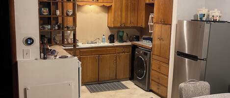 Una cucina compatta con mobili in legno, un frigorifero in acciaio inossidabile, una lavatrice e un’area pranzo con tavolo e sedie.