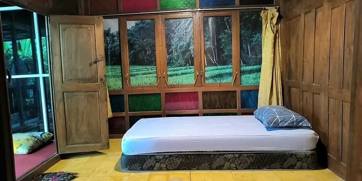 A room with a bed, a window with a view of greenery, and a wooden door.