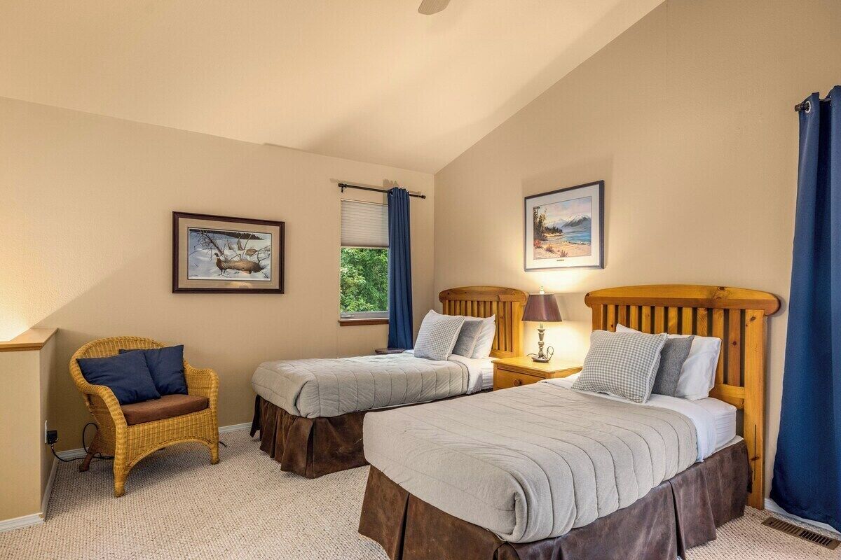 A room with two beds, a chair, and two windows with curtains.