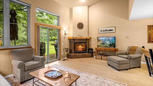 A spacious living room with a fireplace, comfortable seating, and a large window offering a view of the outdoors.