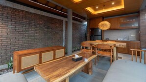 A modern kitchen with wooden cabinets, a dining area with a wooden table and chairs, and a brick wall.