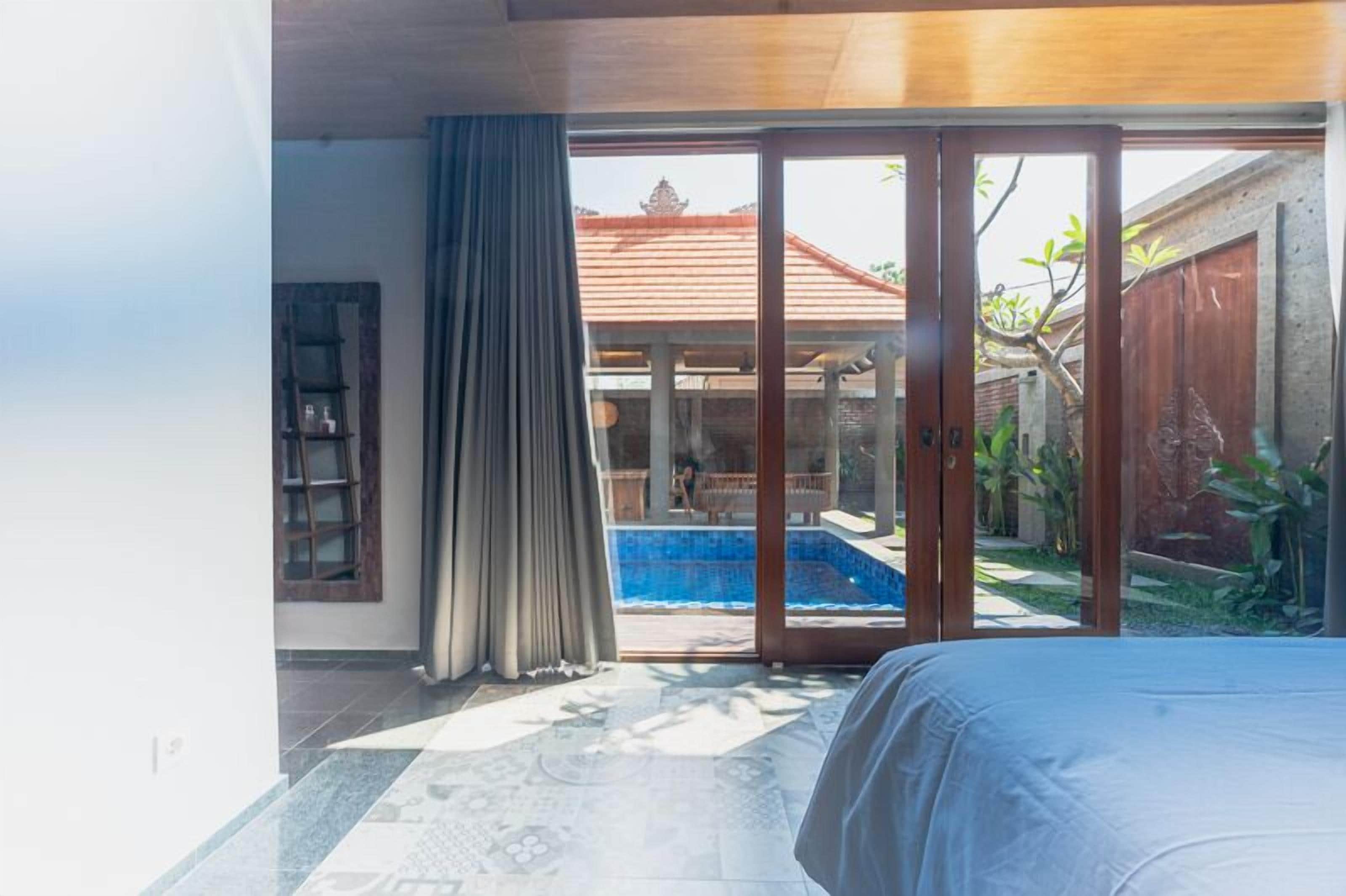 A bedroom with a bed, a sliding glass door leading to a pool area, and a view of a traditional building.
