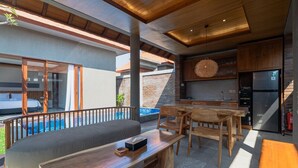 A modern outdoor living area with a pool, wooden furniture, and a kitchen area with a refrigerator.