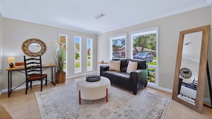 A living room with a black leather sofa, a round wooden chair, a white ottoman, and a large mirror.