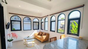 A spacious room with a large marble table, a sofa, and multiple arched windows providing natural light. - Crystal Flow Guest House & Apartment Canggu (Canggu)