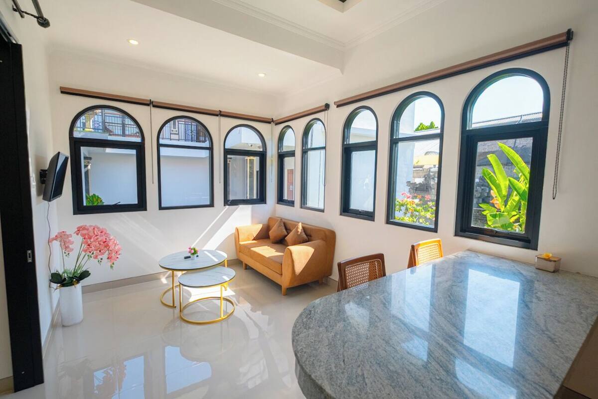 A spacious room with a large marble table, a sofa, and multiple arched windows providing natural light.