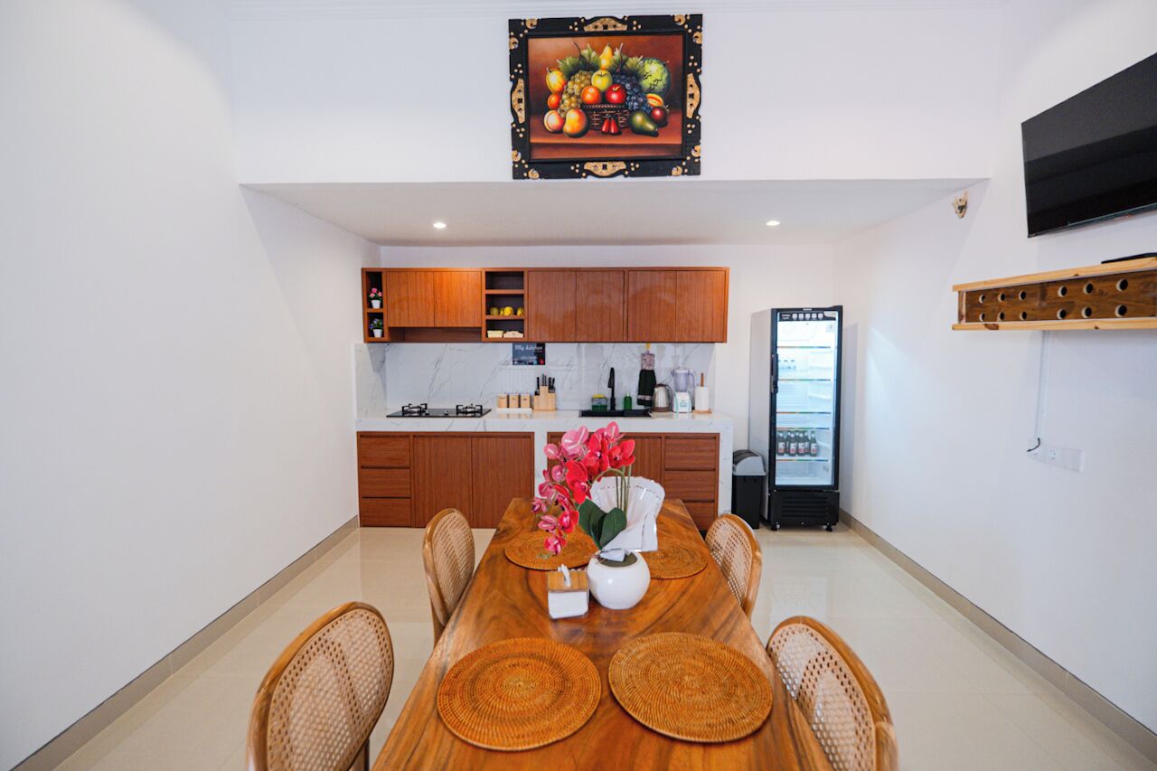 Una cocina moderna con armarios de madera, un refrigerador empotrado y un comedor con mesa de madera y individuales tejidos.