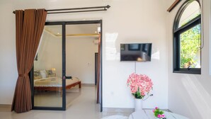 A modern bedroom with a sliding glass door, a bed, a TV, and a potted plant. - Crystal Flow Guest House & Apartment Canggu (Canggu)