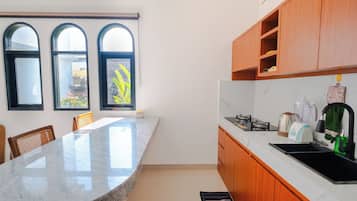 Una cocina con encimera de mármol, armarios de madera y un lavamanos negro. Hay tres ventanas con arcos y vistas al verdor exterior.