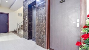 A hotel lobby with a marble reception desk, a staircase, and a door marked with the number 207. - Hotel Gulab Vatika (Jaipur)