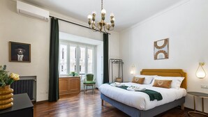 Une chambre d’hôtel avec un grand lit, un lustre, une vue sur la ville et un fauteuil vert.