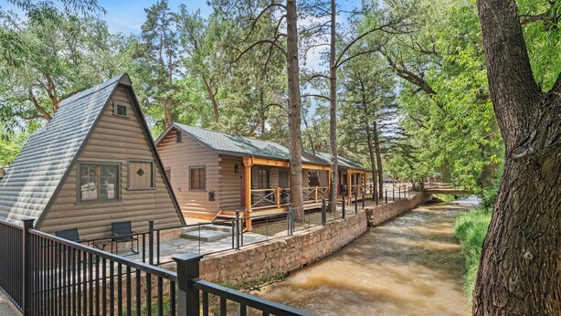 A log cabin with a stone retaining wall and a wooden deck overlooking a river.