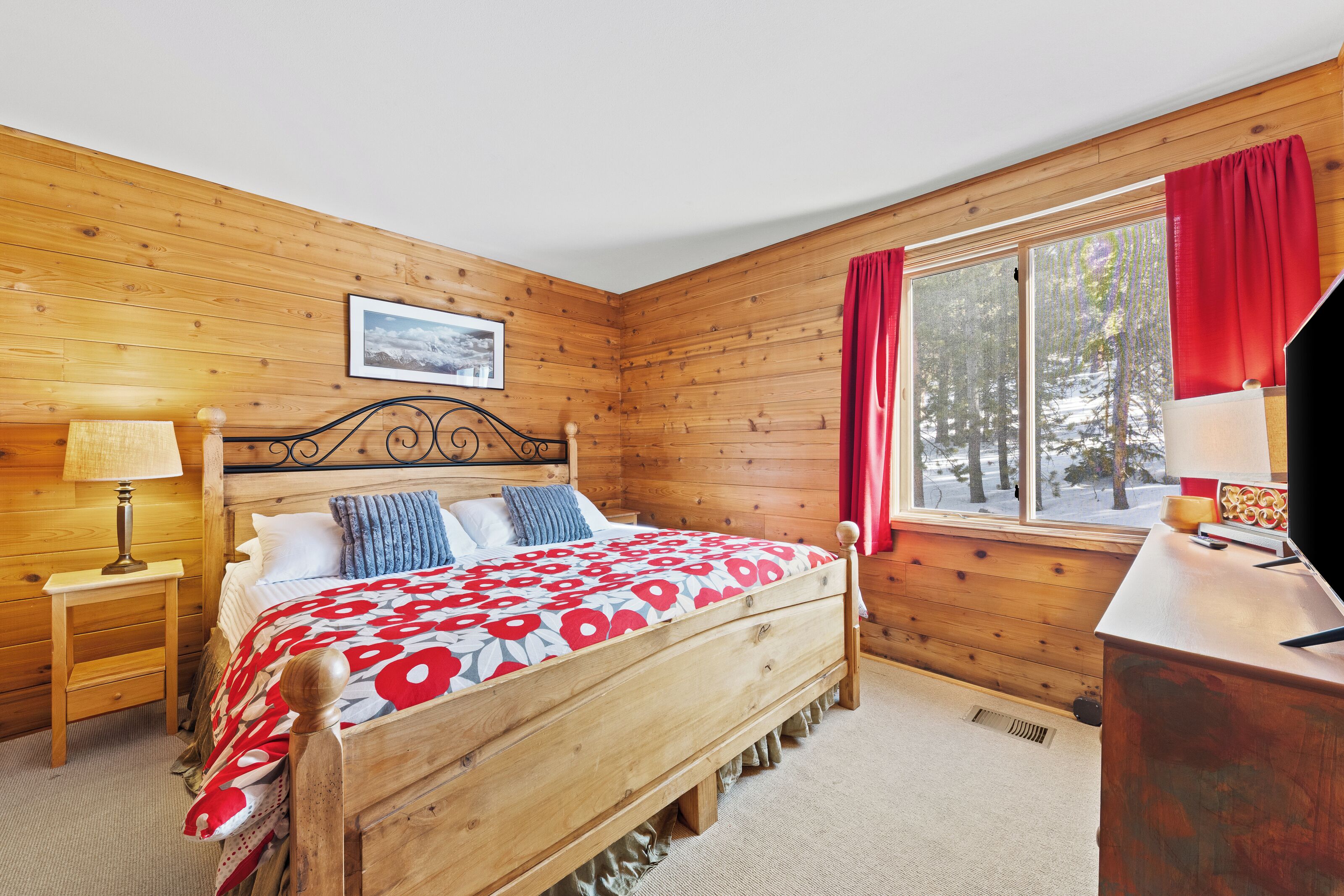 Un dormitorio con paneles de madera, una cama, una mesita de noche, una ventana con vistas a árboles y un cuadro en la pared.