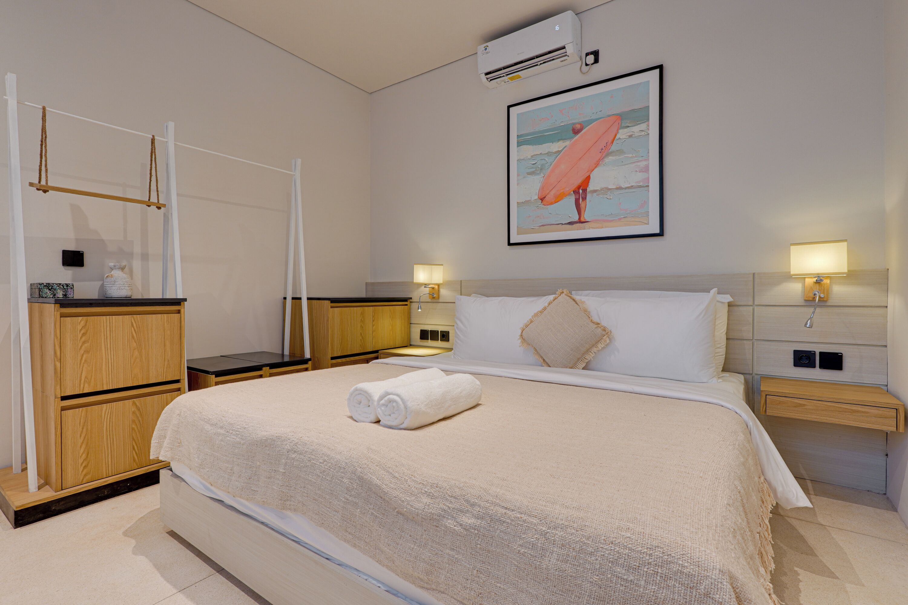 Habitación de hotel con una cama grande, lámparas de noche, una mesita de madera, una pequeña mesa y un aire acondicionado instalado en la pared.