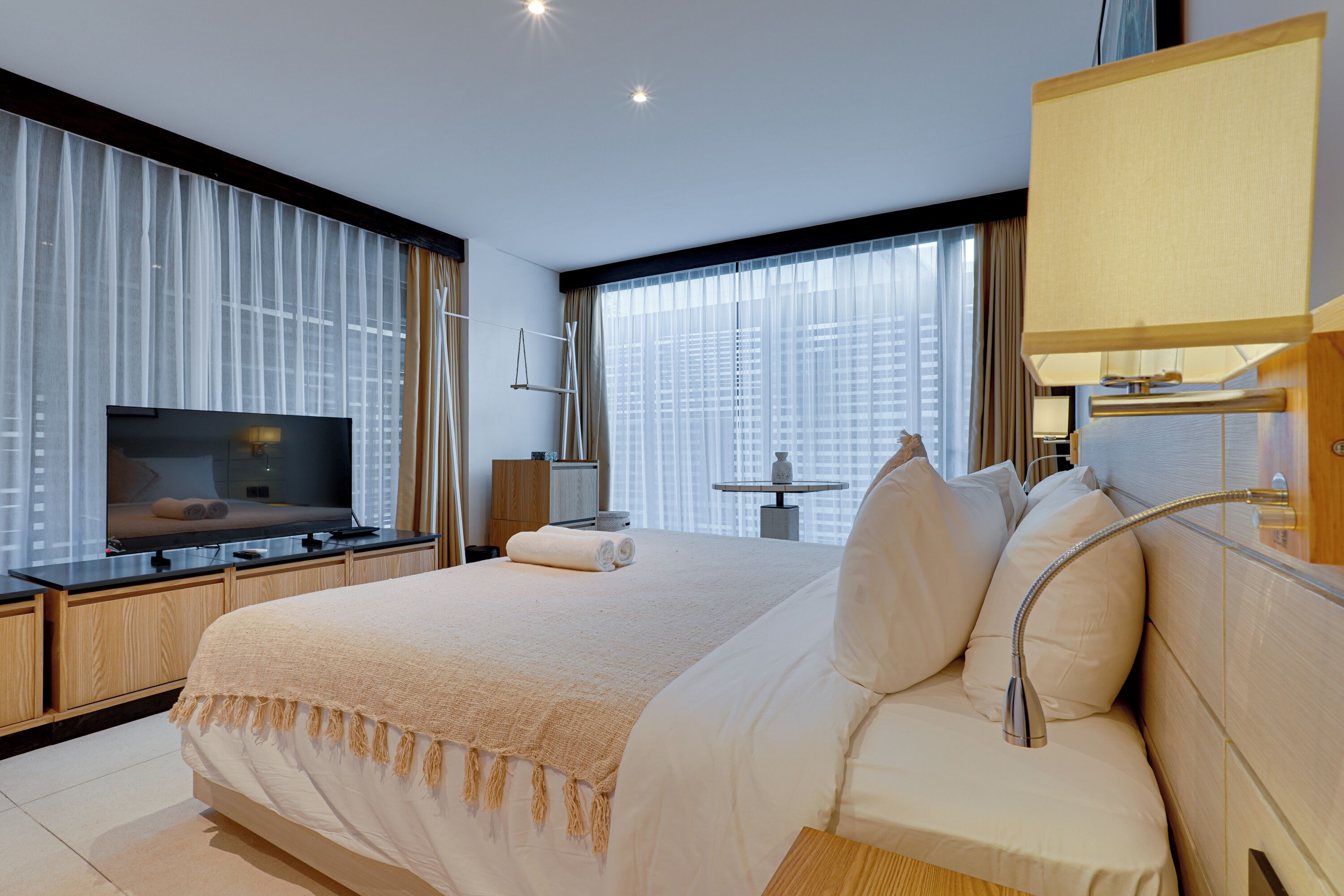 Une chambre d’hôtel moderne dotée d’un grand lit, d’un téléviseur à écran plat, d’un bureau avec une lampe et offrant une vue sur la ville grâce à de grandes fenêtres.