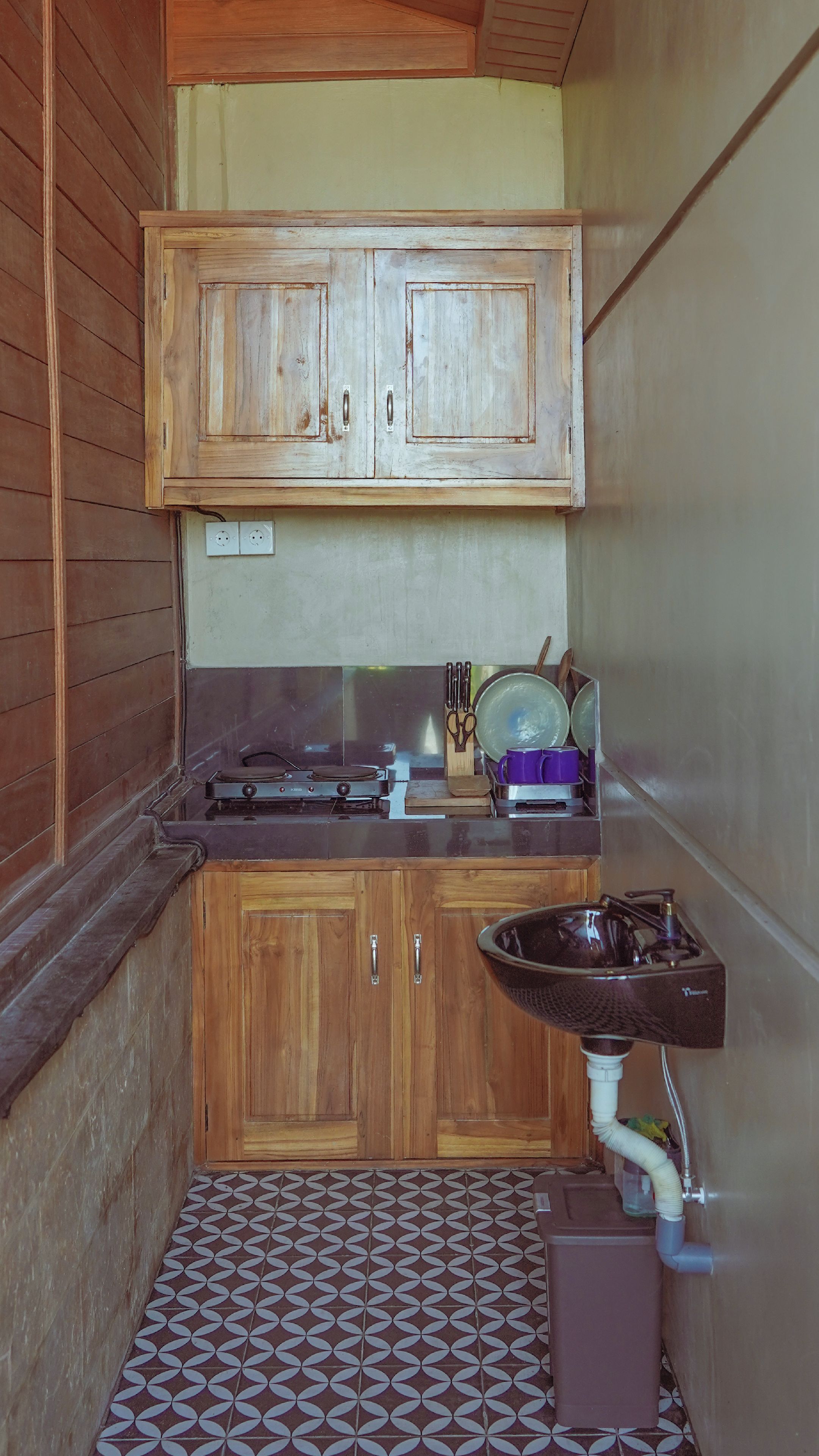A compact kitchen with wooden cabinets, a gas stove, a sink, and a patterned floor.