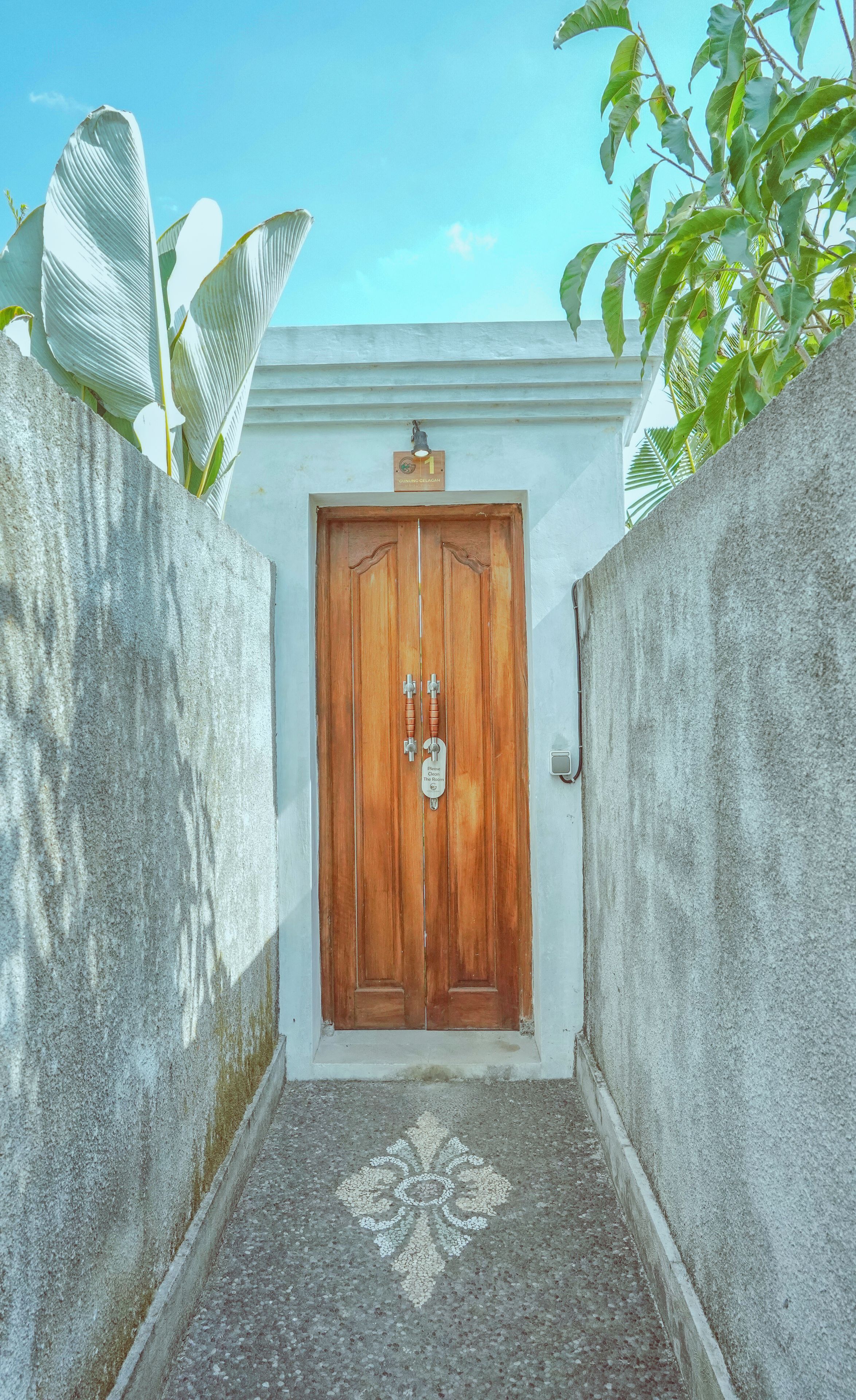 A wooden door with a sign above it, a concrete wall, and a patterned floor leading to the door.