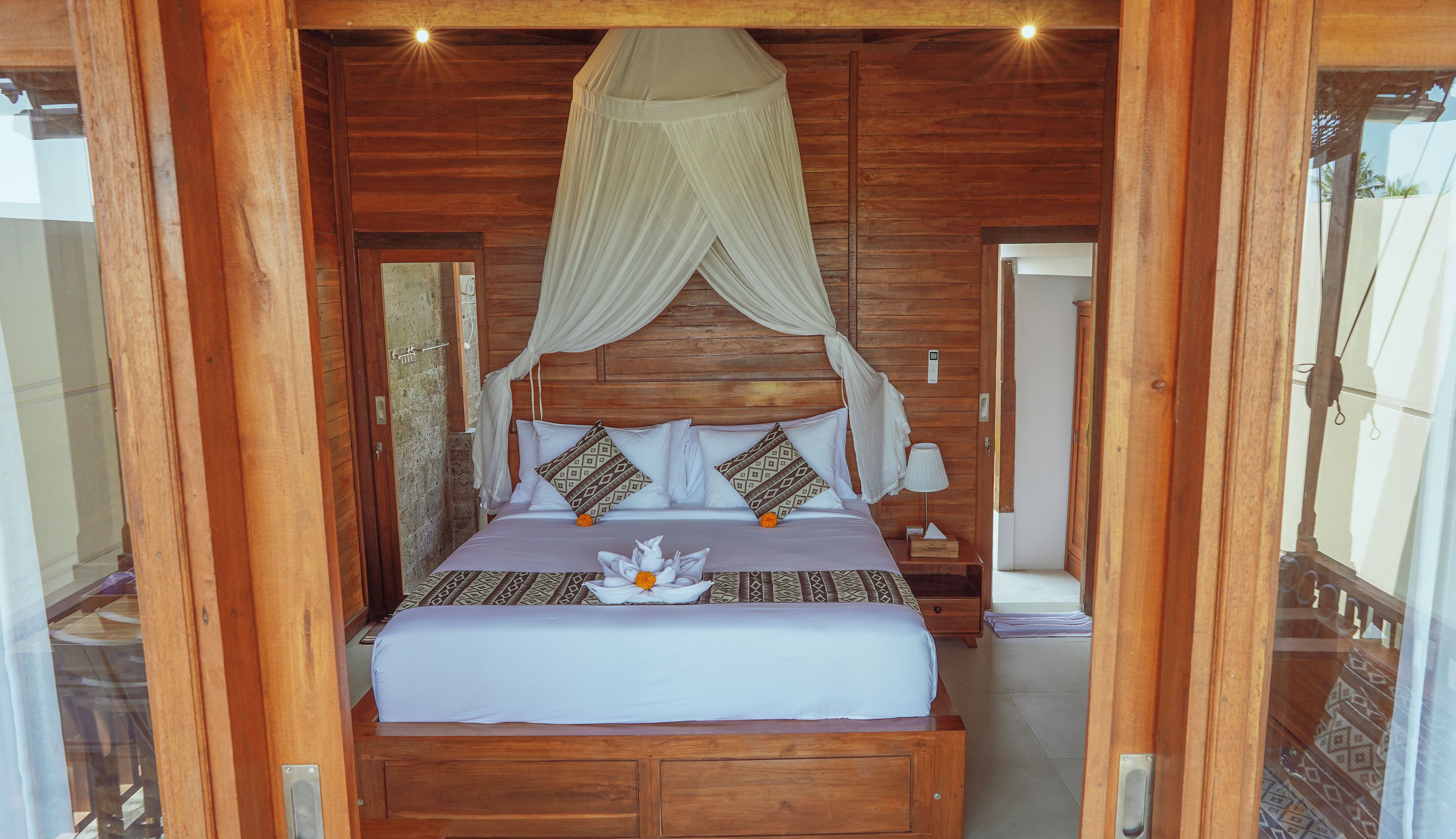 A wooden-framed bedroom with a canopy bed, a bedside table with a lamp, and a nightstand with a tissue box.