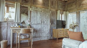 A rustic room with a wooden desk, a chair, a television on a wooden cabinet, and a large window with curtains.