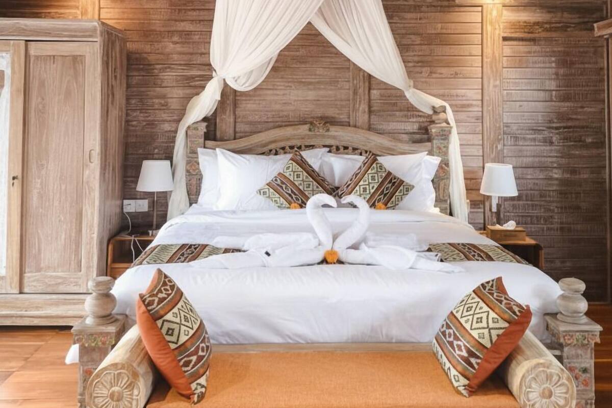 A wooden four-poster bed with a canopy, white bedding, and decorative pillows.