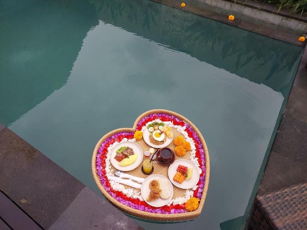 Una bandeja con forma de corazón, comida y flores junto a una piscina.