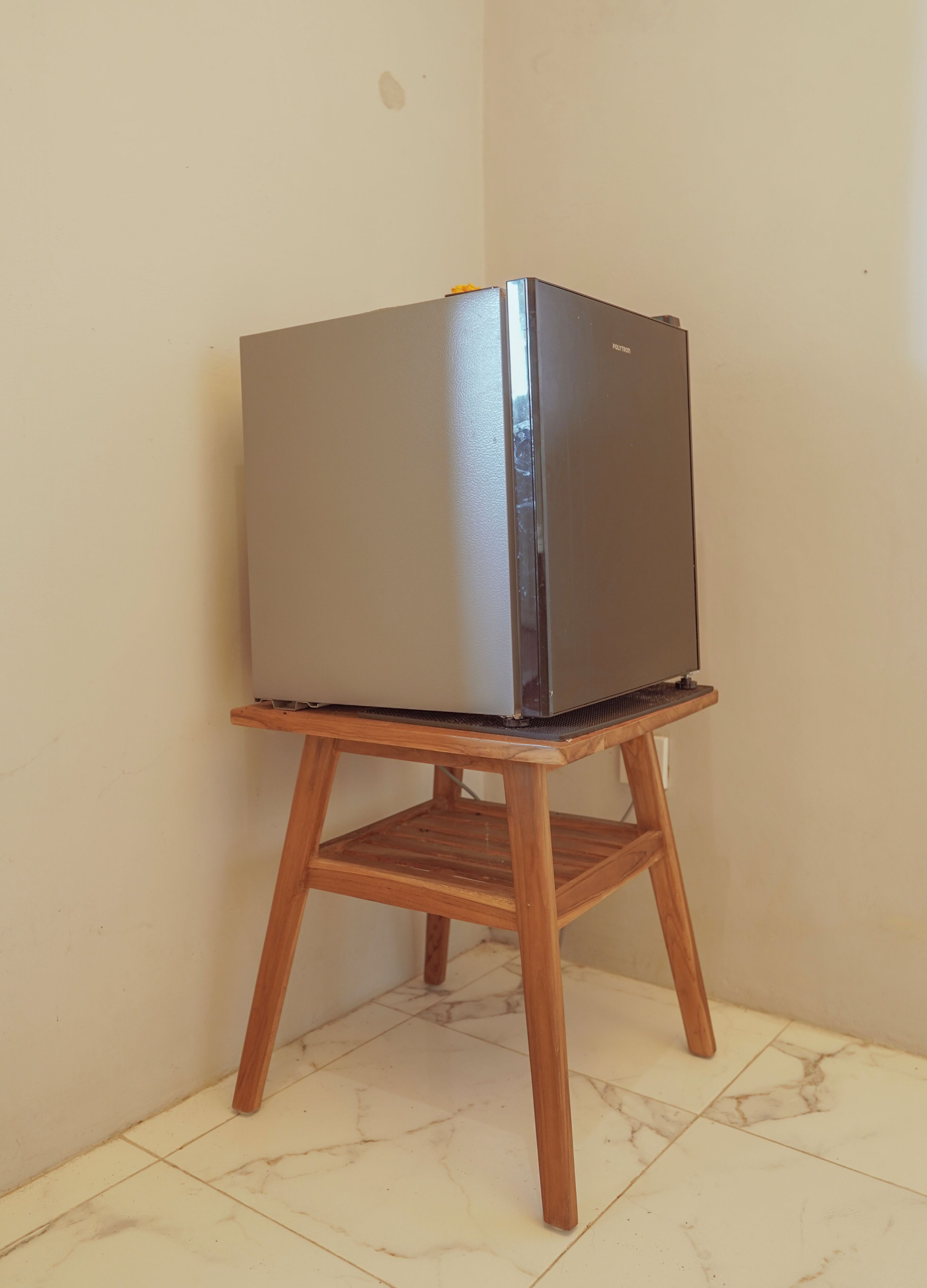 Ein Kühlschrank auf einem Holzgestell in einer Raumecke mit Fliesenboden.