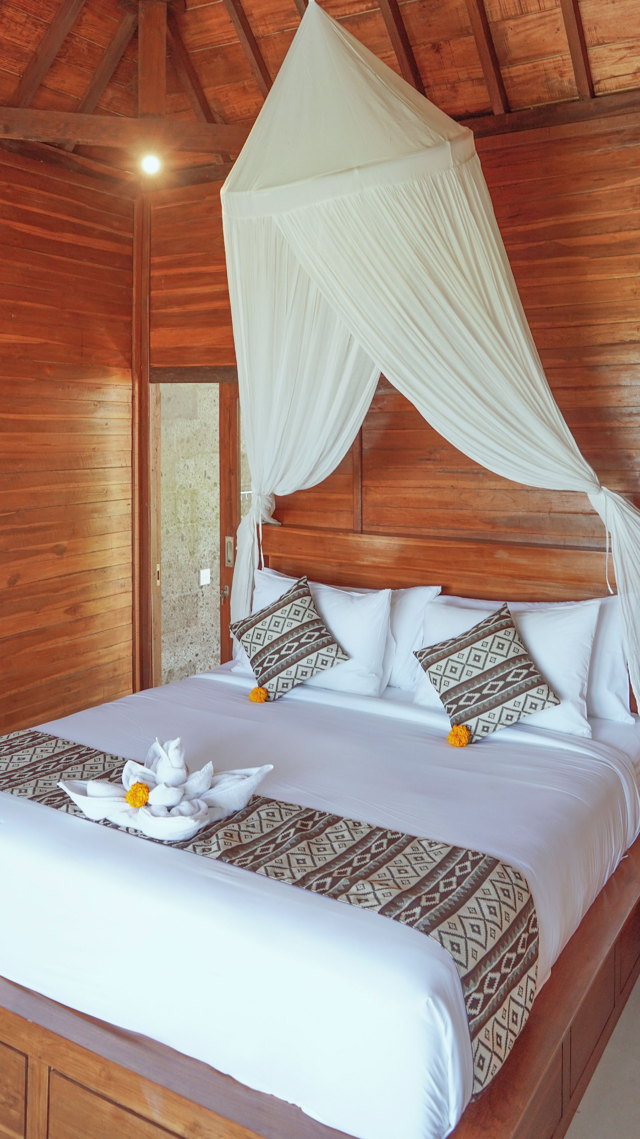 A wooden room with a bed, a canopy, and a patterned bedspread.