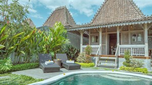 A traditional house with a tiled roof, a porch with white railings, and a swimming pool.