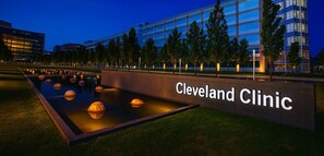 Un bâtiment moderne, sur lequel on peut lire l’inscription « Cleveland Clinic », et un espace paysager agrémenté d’un élément décoratif aquatique.